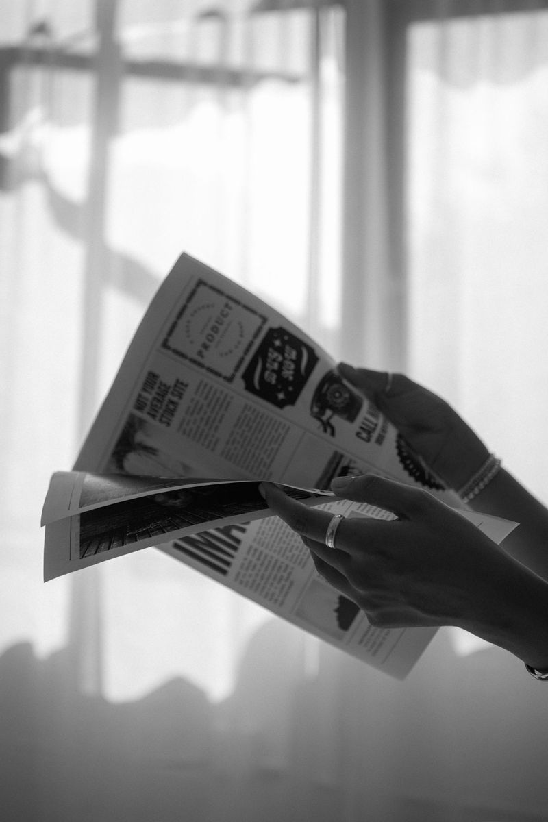 Black-and-white close-up of hands turning the pages of a printed publication.