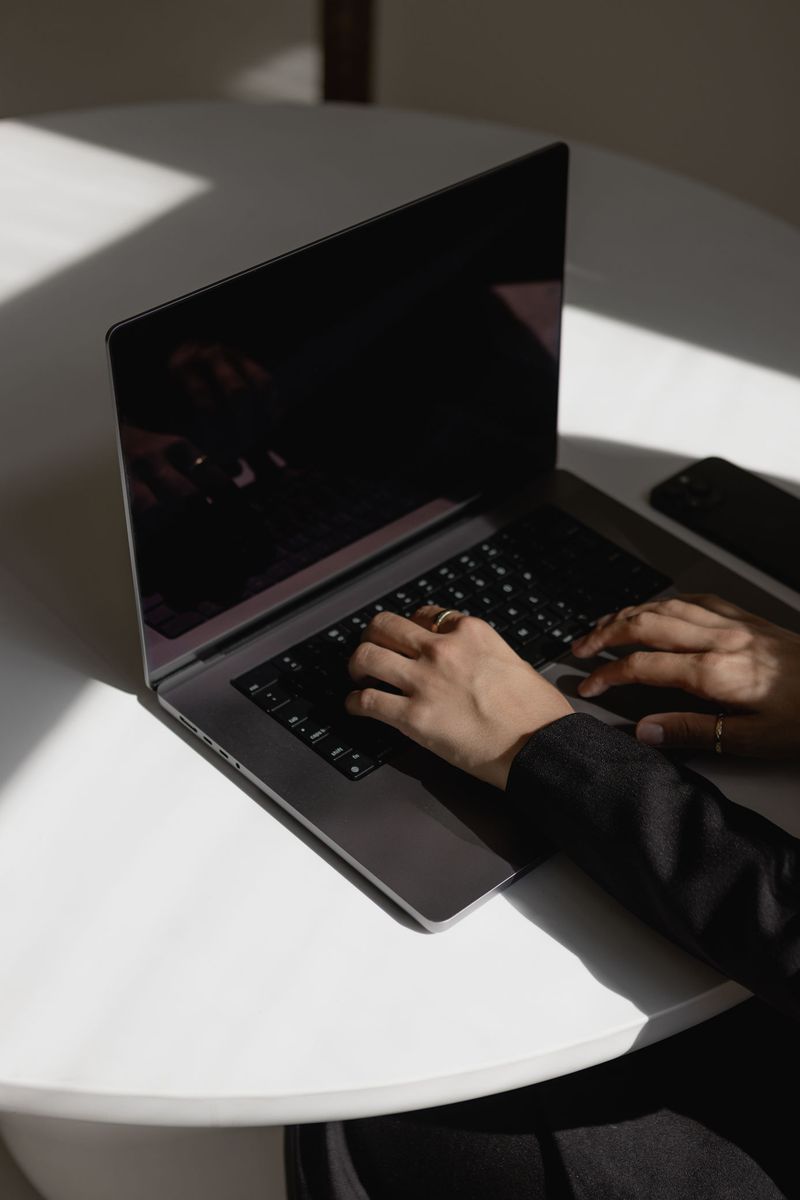 Hands typing on a laptop in hard window light.