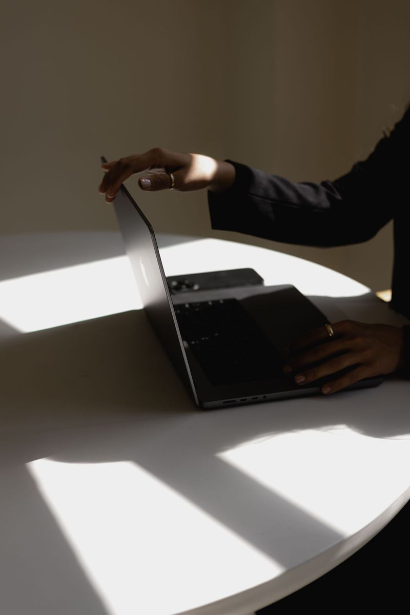 A hand opening a laptop lid in a band of sunlight.